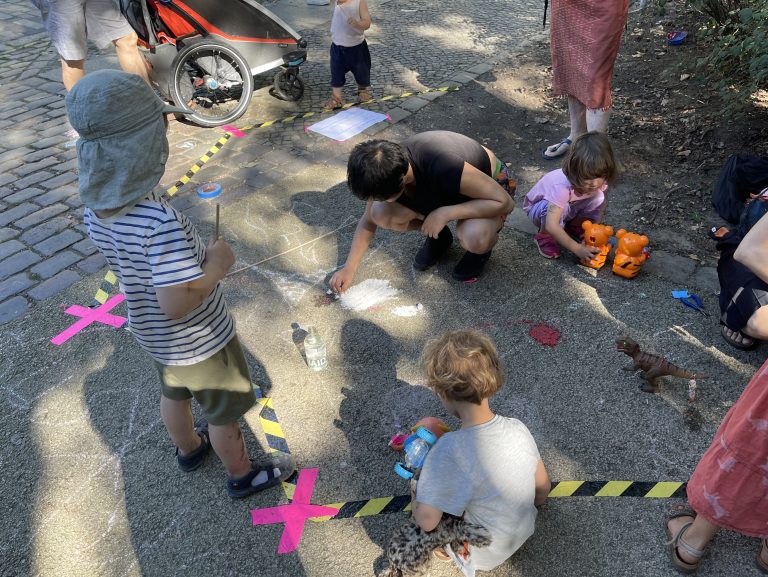 Kinder malen auf der Straße mit Kreide um eine verkehrsberuhigte Zone zu erkunden.
