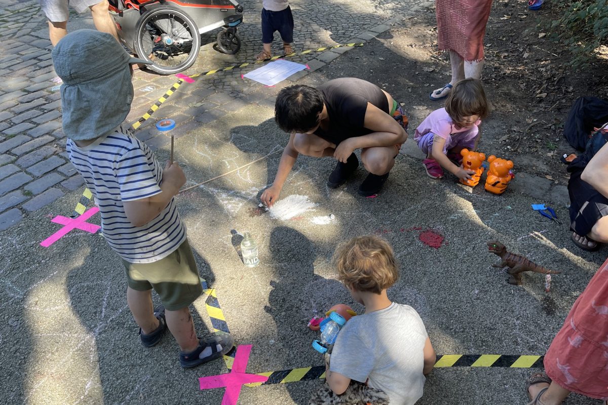 Kinder malen auf der Straße mit Kreide um eine verkehrsberuhigte Zone zu erkunden.